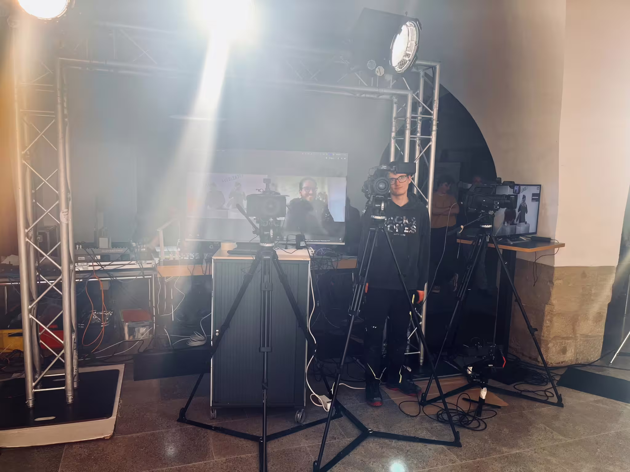 AUFBLENDE 2026 Eventfoto: Kameratechnik und Scheinwerfer hinter Tripods, Techniker und Monitor mit Livestream im Studio